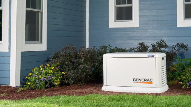 A whole-home Generac generator integrated into landscaping besides a blue exterior.